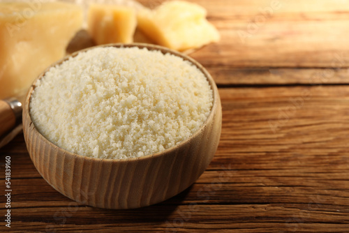 Bowl with grated parmesan cheese on wooden table, closeup. Space for text