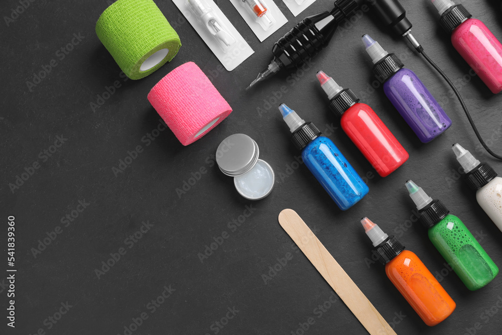 Flat lay composition with tattoo equipment on black table. Space for text