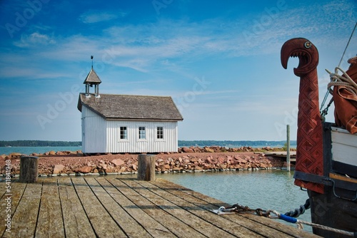 Fotografia Small wooden church on an island with a viking boat at the docks with a dragon's