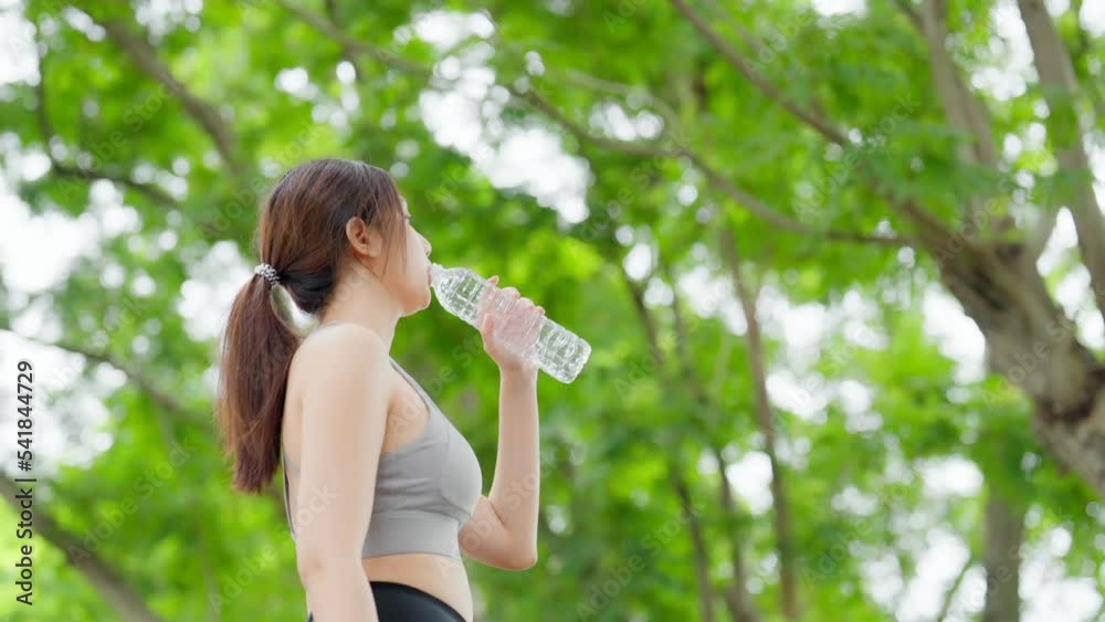Young asian woman drinking water from a bottle while taking a break during her workout. Happy adolescence female working out in the park and taking rest a break to drink water Young asian woman drinking water from a bottle while taking a break during her workout. Happy adolescence female working out in the park and taking rest a break to drink water