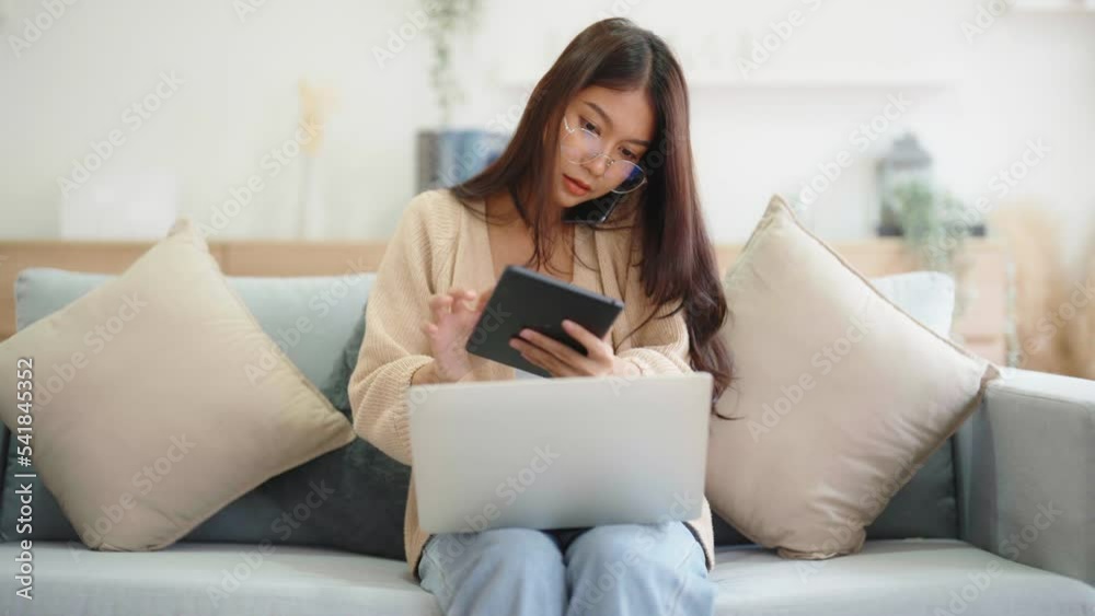 Young asian woman using computer laptop, tablet and mobile smartphone while seated on couch at home Young asian woman using computer laptop, tablet and mobile smartphone while seated on couch at home