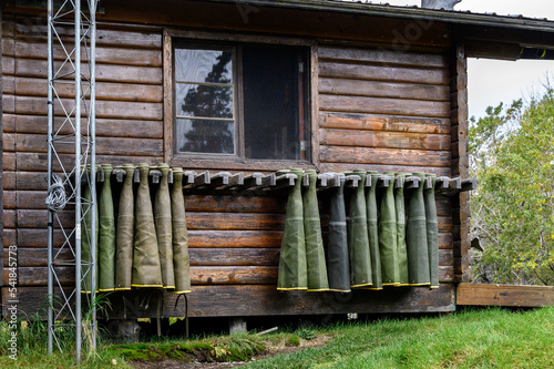 Collection of hip waders hanging up drying outside on a rustic wood cabin
 photo