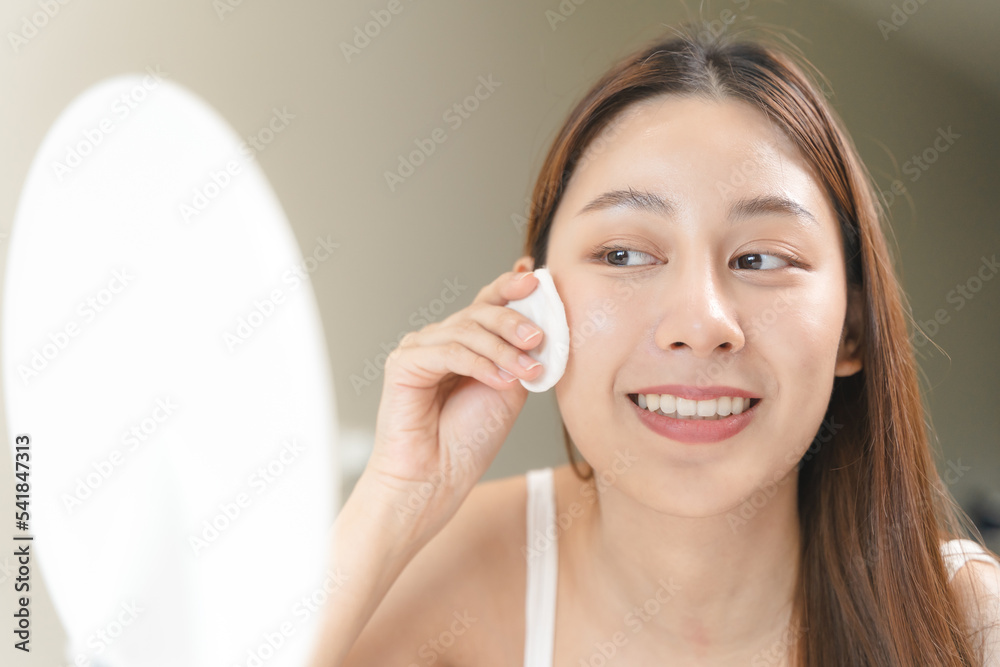 Happy asian woman looking at mirror and using cotton pad clean make up on her face Happy asian woman looking at mirror and using cotton pad clean make up on her face