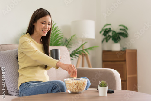 Leisure activity concept, Young woman grabbing popcorn in bowl and drinks coffee while watching tv