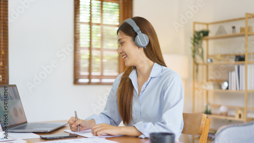 Business at home concept, Businesswoman wear headphone to meeting in video call and taking notes