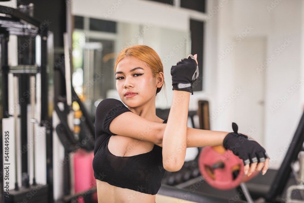 A young woman in a black crop top does a shoulder stretch before a workout session at the gym. Warming up upper body properly. A young woman in a black crop top does a shoulder stretch before a workout session at the gym. Warming up upper body properly.