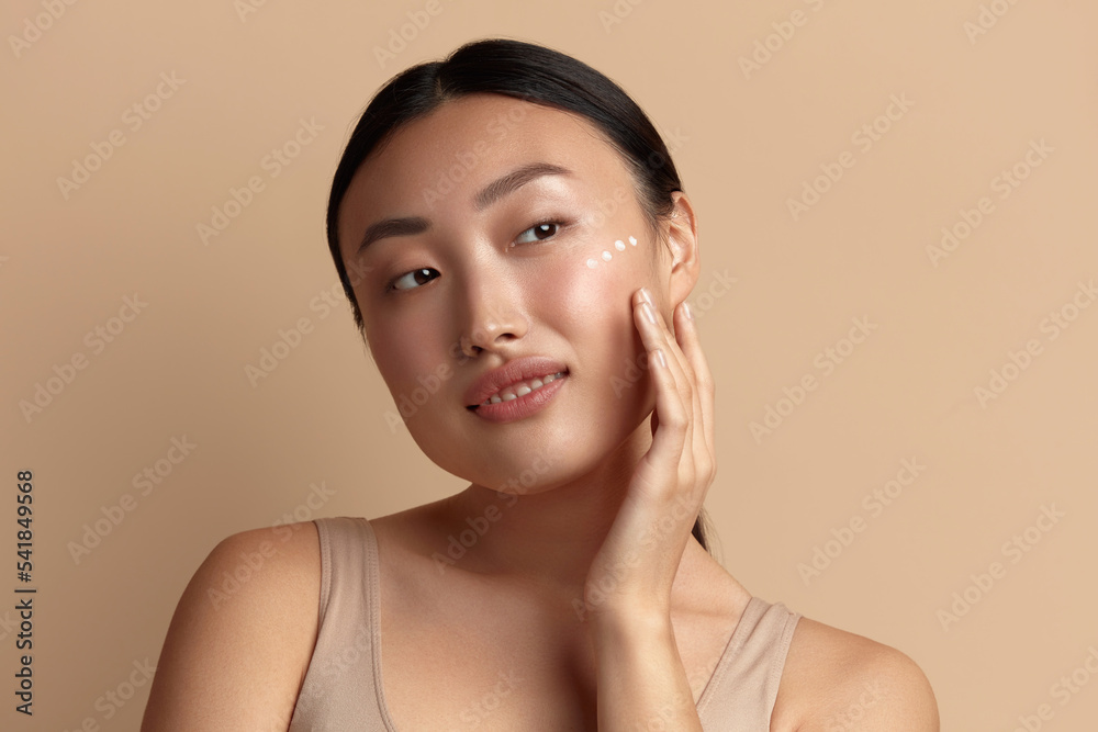 Skin Care Woman Applying Cream on Cheek. Closeup Of Asian Smiling Girl