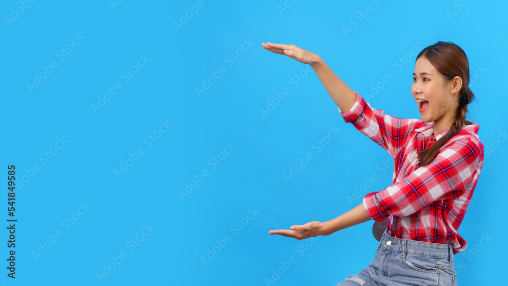 Women smiling and holding an object both hands with empty space on isolated light blue background Women smiling and holding an object both hands with empty space on isolated light blue background