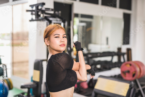 A pretty and alluring woman in a sheer top does a shoulder stretch before a workout session at the gym. Warming up upper body properly. © Mdv Edwards