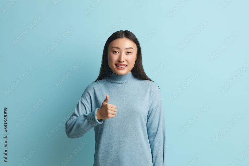 Smiling Woman Showing Big Fingers Isolated. Asian Girl Looking at Camera with Toothy Smile and Showing Thumb Up, Approval Sign, Satisfied with Service, Good Feedback. Indoor Shot on Blue Background Smiling Woman Showing Big Fingers Isolated. Asian Girl Looking at Camera with Toothy Smile and Showing Thumb Up, Approval Sign, Satisfied with Service, Good Feedback. Indoor Shot on Blue Background