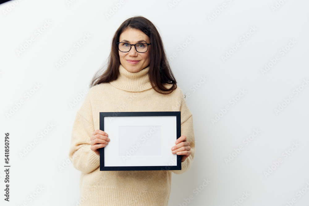 attractive woman with long dark hair, smiling cutely looking at the camera, standing in a sweater with a black frame in her hands on a light background. Studio photography with space for mockup attractive woman with long dark hair, smiling cutely looking at the camera, standing in a sweater with a black frame in her hands on a light background. Studio photography with space for mockup