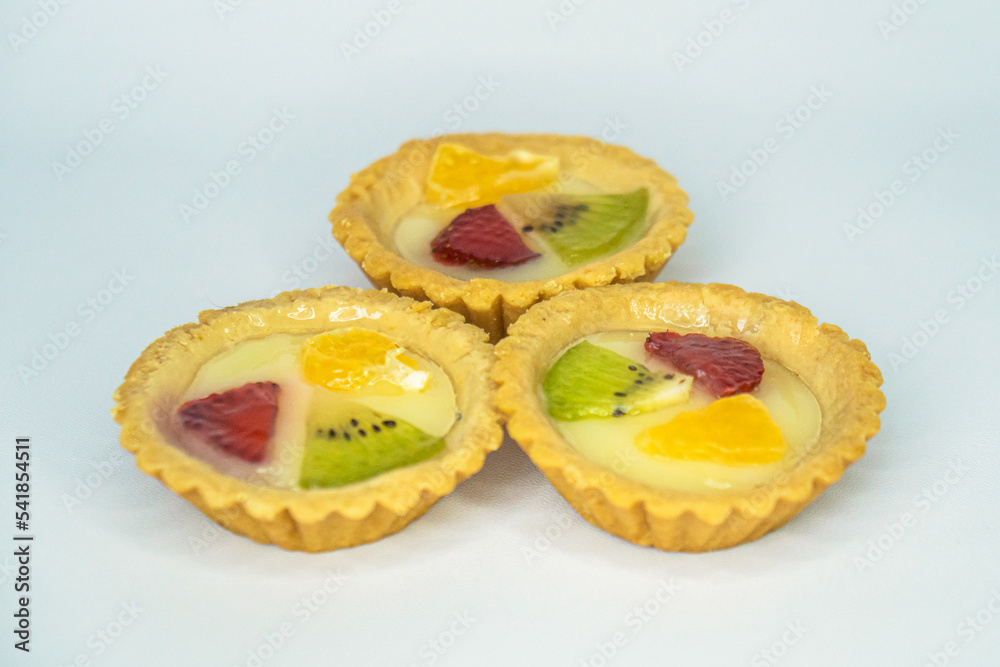 A small plate of a typical Indonesian snack called Pie Susu topped with slices of orange, strawberry and kiwi, served on a white background A small plate of a typical Indonesian snack called Pie Susu topped with slices of orange, strawberry and kiwi, served on a white background