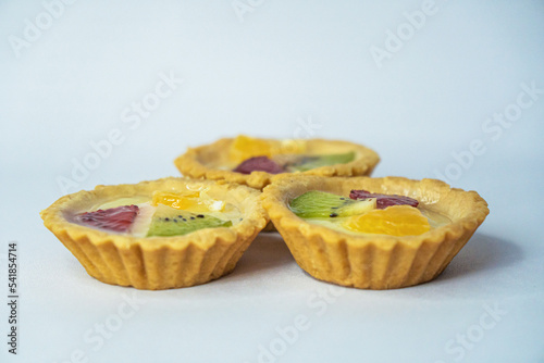 A small plate of a typical Indonesian snack called Pie Susu topped with slices of orange, strawberry and kiwi, served on a white background