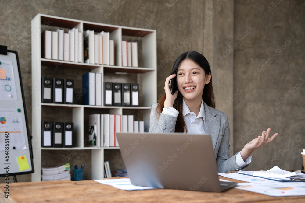 Smiling beautiful Asian businesswoman analyzing chart and graph showing changes on the market and holding smartphone at office. Smiling beautiful Asian businesswoman analyzing chart and graph showing changes on the market and holding smartphone at office.