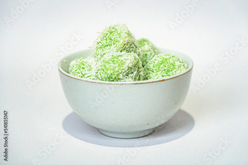 A traditional Indonesian snack called klepon, made from green glutinous rice and inside there is brown sugar, small round shape with grated coconut topping, served in a small bowl on a white backgroud