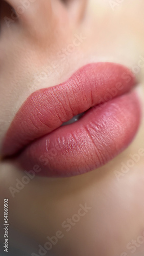 permanent makeup on the lips of a young woman of a delicate peach shade close-up  a girl after a cosmetic procedure with smooth and clean healthy skin.