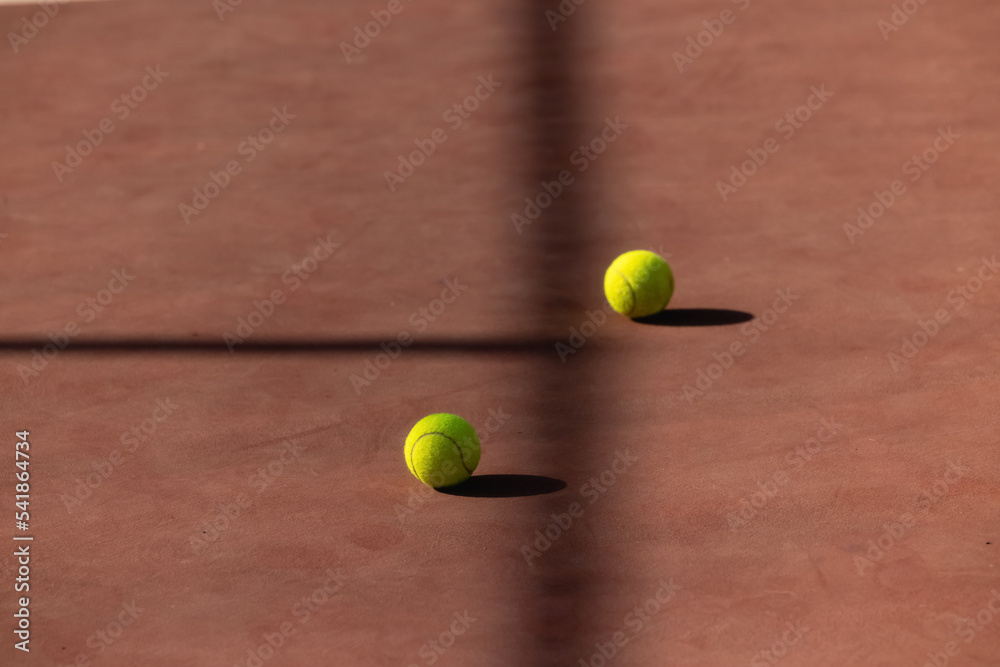 Tennis ball on clay court two separated by shadow