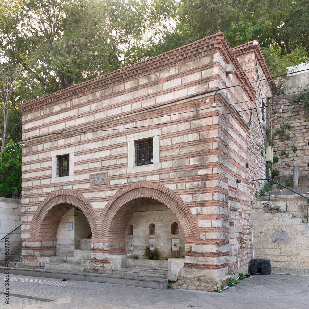 Fototapeta premium Kanuni Sultan Suleyman Fountain or Cesmesi, a classical fountain in Alaca Tekke Street, near Eyup Sultan Mosque, with traditional red and white stone bricks, and two big arches, Istanbul, Turkey