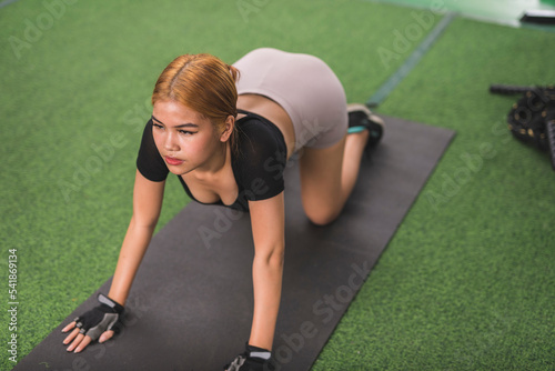 A sexy young asian woman does a cat and dog stretch. Doing yoga or warming up for a workout at the gym.