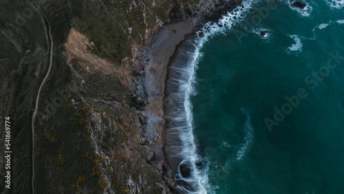 Aerial shot of the coast of a sea with waves by rocky mountain