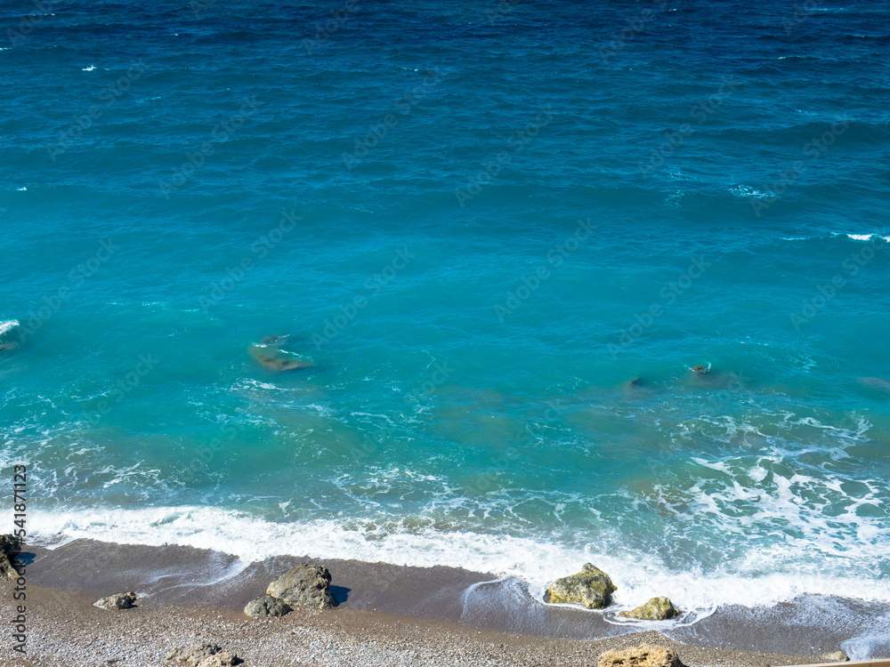 Obraz premium Beautiful and deserted beach on the west coast of Rhodes near Kamiros. Turquoise sea water, blue cloudless sky, pebble beach. Tourism and vacations concept. Space for text.