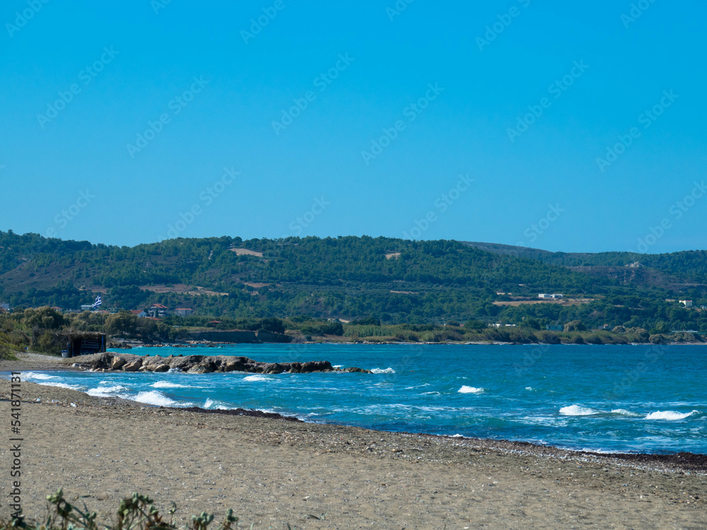 Beautiful and deserted beach on the west coast of Rhodes near Kamiros. Turquoise sea water, blue cloudless sky, pebble beach. Tourism and vacations concept. Space for text.