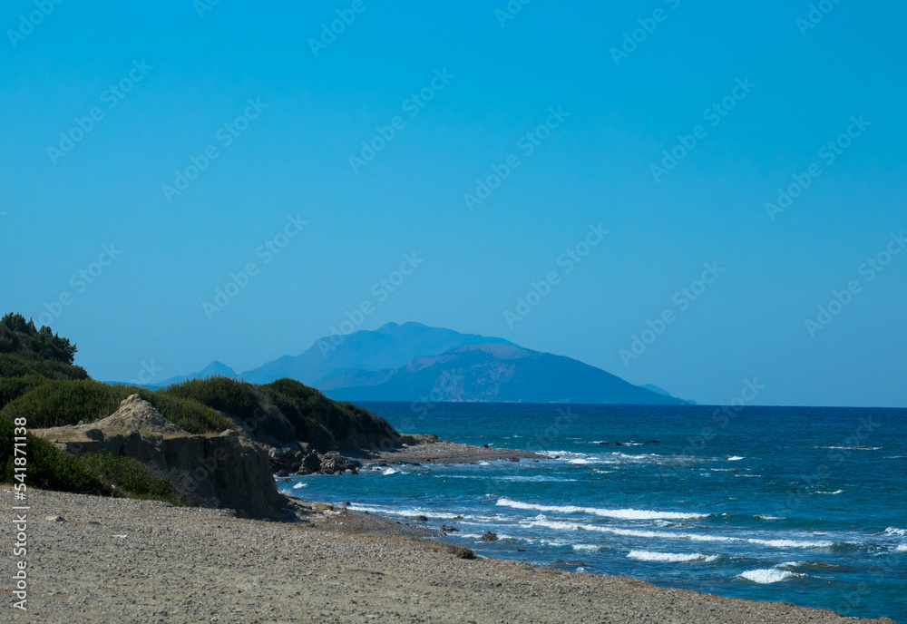 Beautiful and deserted beach on the west coast of Rhodes near Kamiros. Turquoise sea water, blue cloudless sky, pebble beach. Tourism and vacations concept. Space for text.