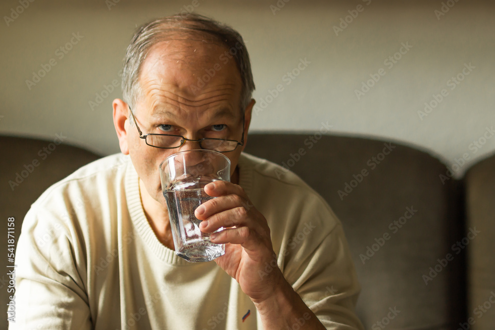 Caucasian senior man in white sweater take capsule and drinking clear water from glass on sofa at home, feels like sick. Caucasian senior man in white sweater take capsule and drinking clear water from glass on sofa at home, feels like sick.