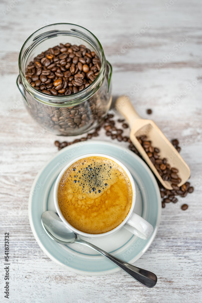 Freshly brewed coffee mug and glass jar with roasted coffee beans on a vintage table. Freshly brewed coffee mug and glass jar with roasted coffee beans on a vintage table.