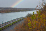 Colorful autumn landscape, view of the river with a road and a rainbow sky. Empty streets and roads. City view from above with fallen leaves, trees. Nature of the autumn season.