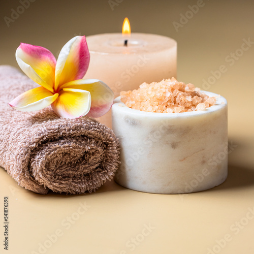 Minismalist spa salon and wellness centre concept .Burning candles, sea salt scrub , frangipani flower and towel on beige background.Copy space