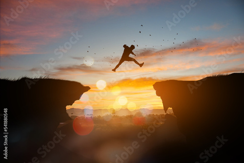 Men jump cliff sun light over silhouette, man is representative of success in the past and gold for the future in 2023