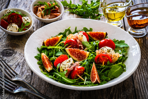 Wallpaper Mural Fresh salad - mozzarella, crudo ham, fig, cherry tomatoes and leafy greens on wooden table
 Torontodigital.ca