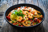 Tom Yum - Thai soup with prawns and rice noodles on black wooden table
