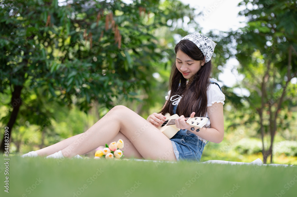 Young Asian woman enjoying and relaxing by playing Ukulele in the park
