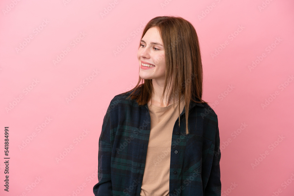 Fototapeta premium Young English woman isolated on pink background looking to the side and smiling