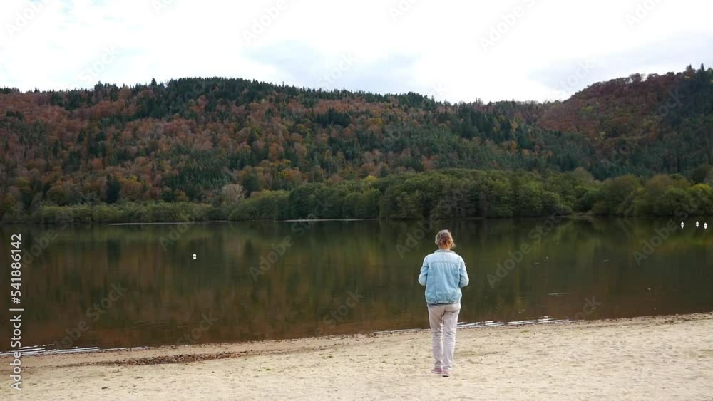 Woman walks by a lake and takes a photo of the mountain and the lake Woman walks by a lake and takes a photo of the mountain and the lake