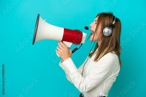 Telemarketer English woman working with a headset isolated on blue background shouting through a megaphone