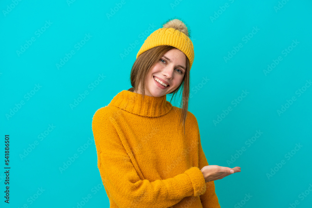 Young English woman wearing winter jacket isolated on blue background presenting an idea while looking smiling towards