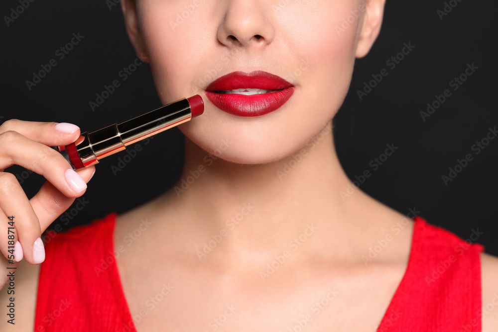 Young woman with beautiful makeup holding red lipstick on black background, closeup Young woman with beautiful makeup holding red lipstick on black background, closeup