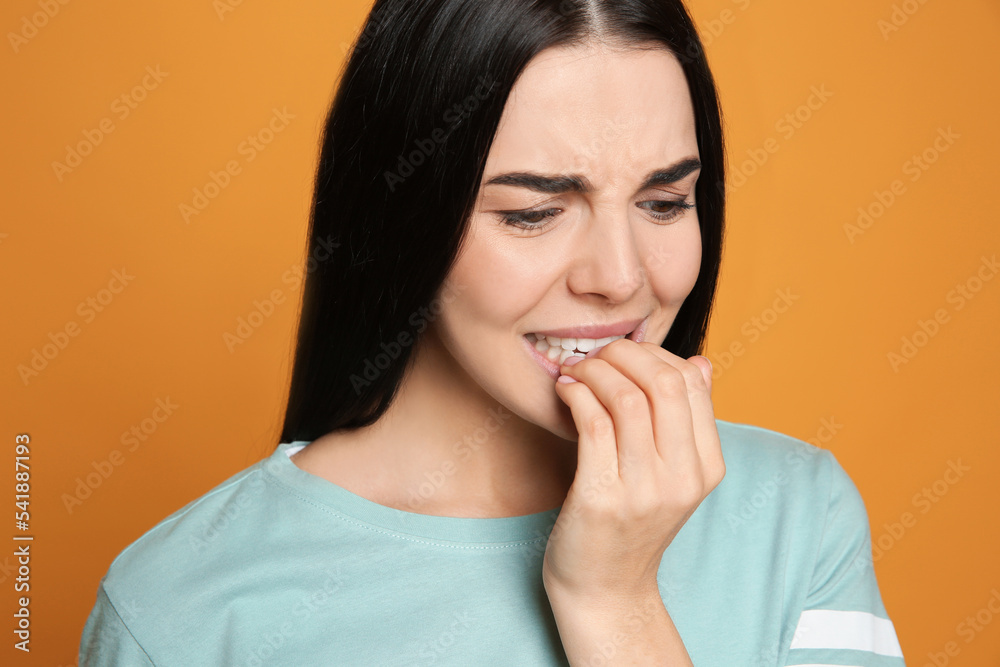 Young woman biting her nails on yellow background Young woman biting her nails on yellow background