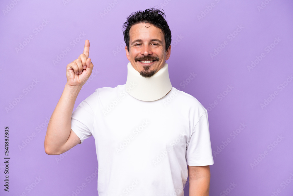 Young caucasian man wearing neck brace isolated on purple background pointing up a great idea