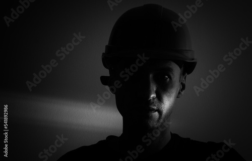 Dirty face of coal miner on a black background. Head of tired mine worker in a hard hat. © Angelov