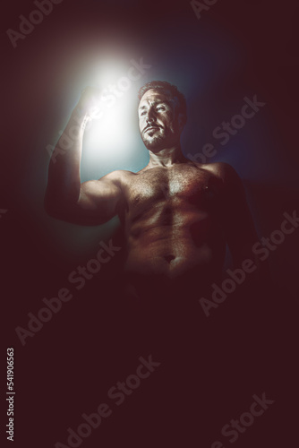 Misterious dark creative artistic portrait of a mature naked man with light in his hand with copyspace. Mental health, phylosophy, spirituality,mindfulness or divinity concept.