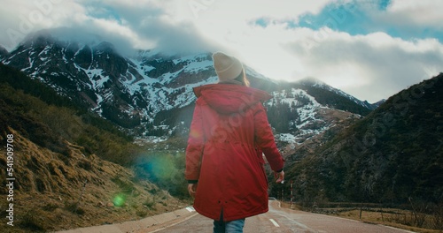 Tourist female in red jacket walk at mountain road on winter vacation travel