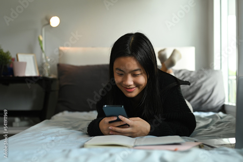 Teenage girl typing text message, chatting online on mobile phone while sitting in cozy bedroom