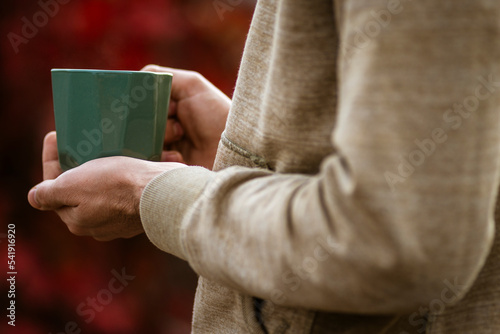 Hands holding green mug Autumn tea mood red oliage blurred bokeh background outdoors Morning Drinking Fall cozy concept, backlit vacation blanket.