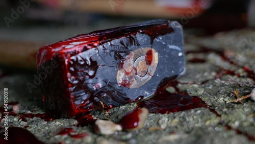 Close up of a bloody lump hammer lying on a grimy concrete floor with blood splattered around it