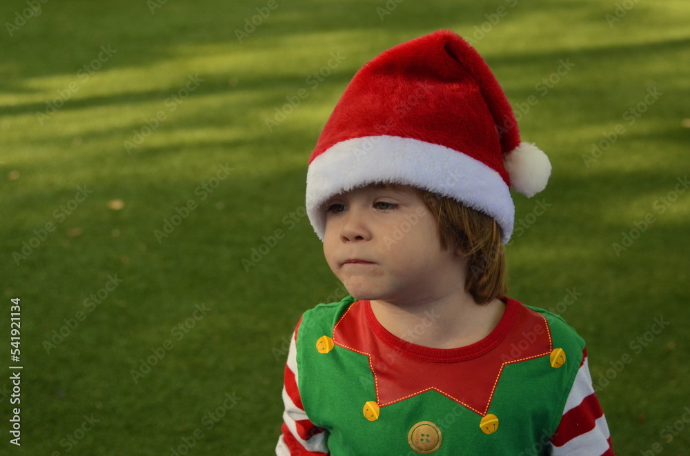 Portrait of a little boy in a Santa Claus hat on a green background. A child dreams of a gift, a boy in an elf costume. Christmas Eve. Portrait of a little boy in a Santa Claus hat on a green background. A child dreams of a gift, a boy in an elf costume. Christmas Eve.