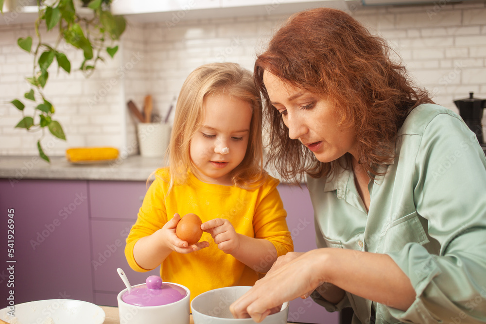 Grandmother and granddaughter cook in kitchen in middle, family pastime, leisure. woman and child make cake in purple, lavender kitchen. bowl